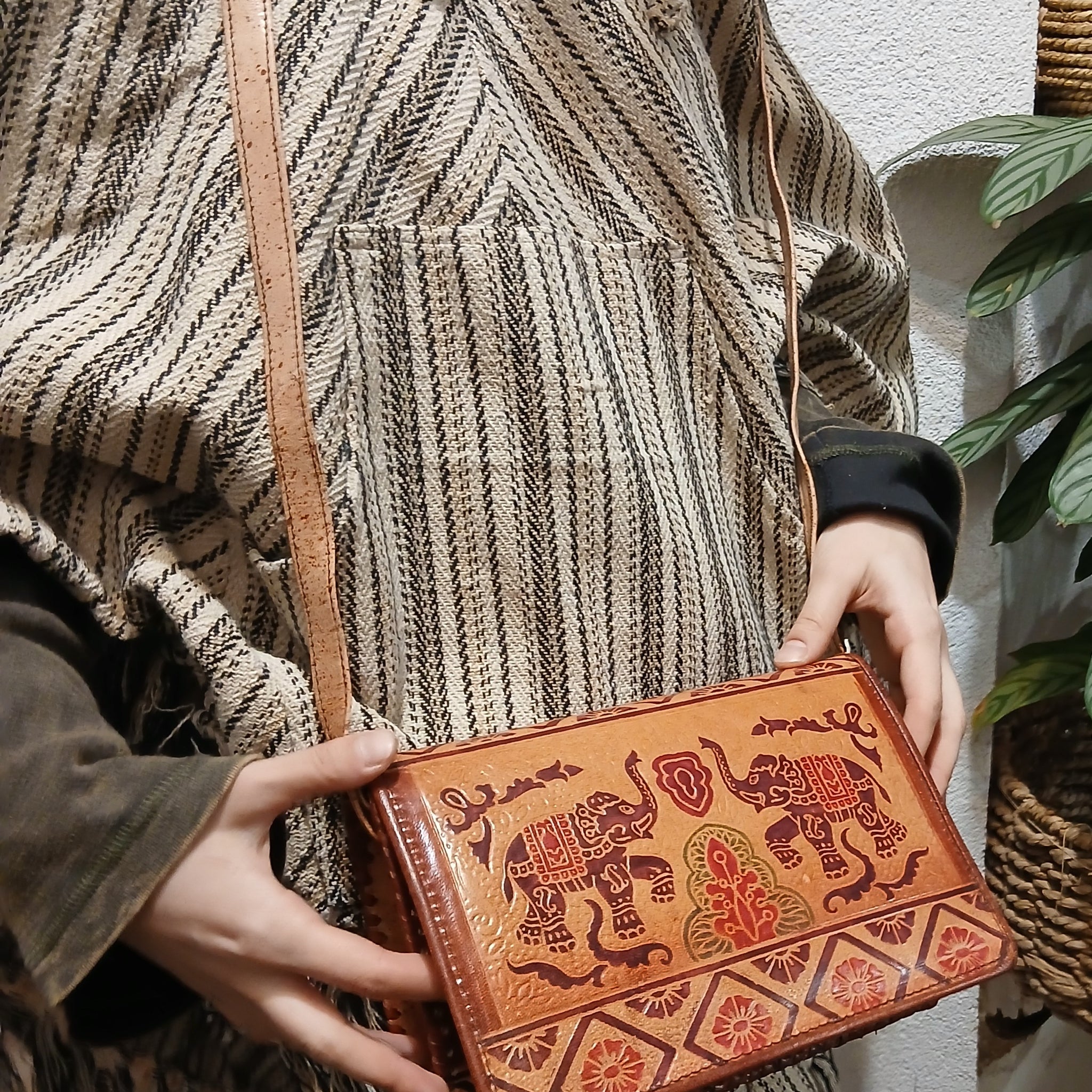 Ručne vyrábaná kožená kabelka s etno vzorom slonov, nosená na ramene ako crossbody.