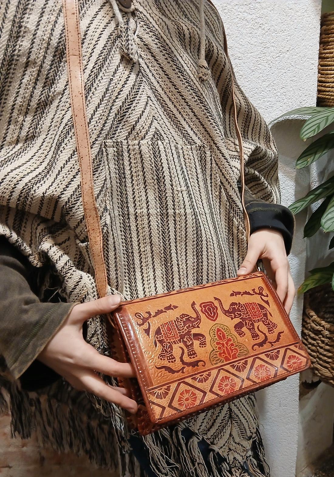 Ručne vyrábaná kožená kabelka s etno vzorom slonov, nosená na ramene ako crossbody.