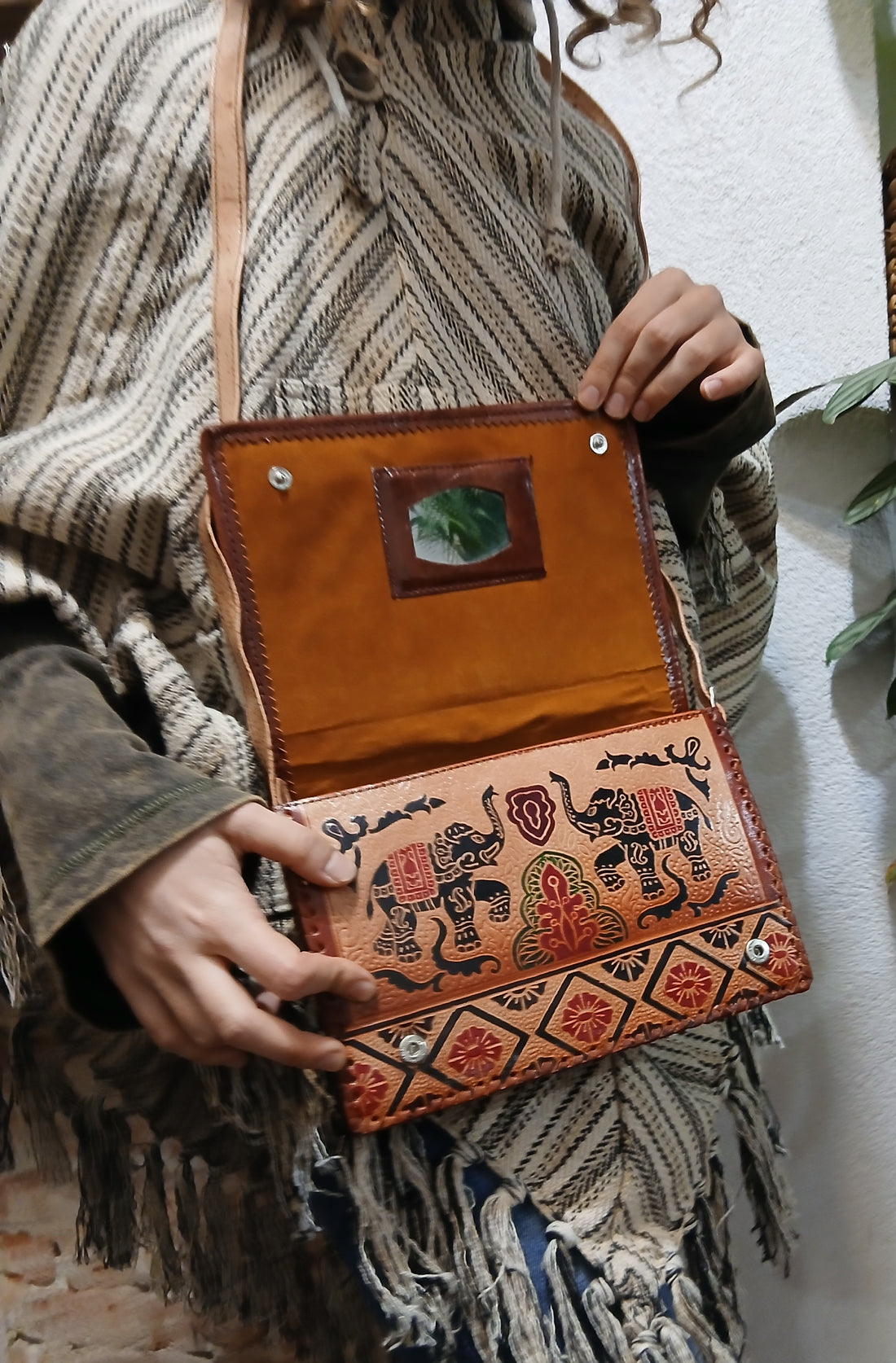 Ručne vyrábaná kožená kabelka s etno vzorom slonov, nosená na ramene ako crossbody.